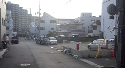 右側に駐車場。正面奥にマンション風の建物。人も通っていない。