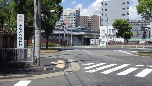 左に『厄除　みなと八幡神社』の看板。正面信号奥に電車の高架。