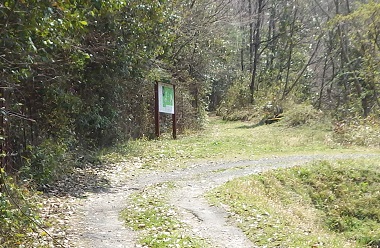 土の道が峠に延びる。左側に説明板